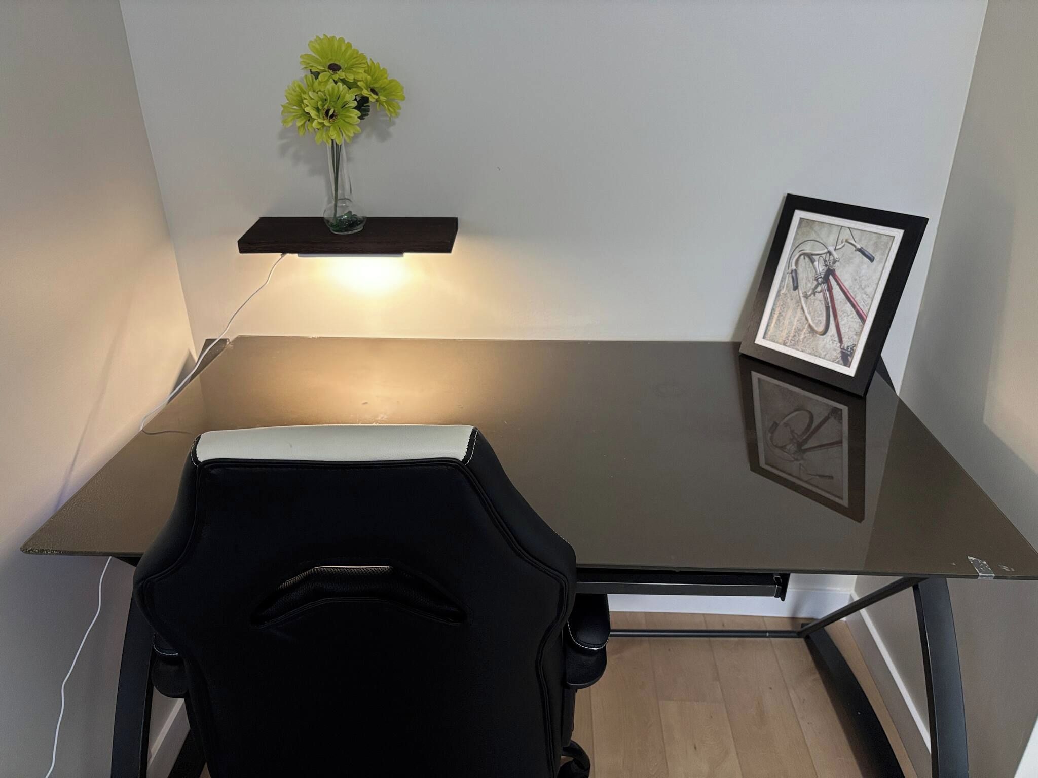 A workspace with a desk, chair, wall-mounted shelf with flowers, and framed pictures.