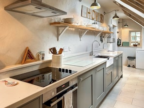 A kitchen with a built-in stove, a sink, and a wooden shelf above the counter. - 2 bedroom accommodation in Fakenham (Fakenham)