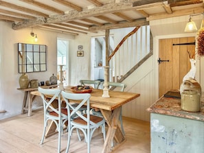 A rustic dining area with a wooden table and white chairs, a staircase, and a wooden door with a deer sculpture. - 2 bedroom accommodation in Fakenham (Fakenham)
