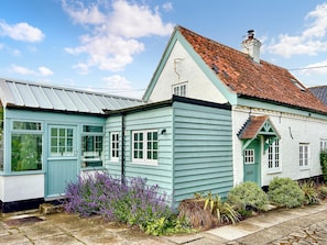 A traditional house with a sloped roof, a front porch, and a garden with various plants. - 2 bedroom accommodation in Fakenham (Fakenham)
