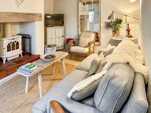 A cozy living room with a sofa, a wooden table with books, a vintage stove, and a mirror. - 2 bedroom accommodation in Fakenham (Fakenham)