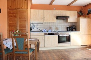 A kitchen with wooden cabinets, a dining table with chairs, and a coffee maker. - House Elke, ground floor apartment (Wieck a. Darß)