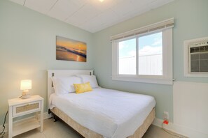 A bedroom with a bed, a nightstand, a lamp, a window, and a wall-mounted air conditioner. - Walk to Beach! Cabin Suite on Lake Huron (Greenbush)