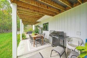 Eine Terrasse im Freien mit einer Holz-Pergola, einem Grill, einem Esstisch mit Stühlen und Topfpflanzen.