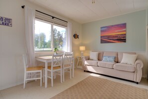 Una sala de estar acogedora con un sofá blanco, una mesa de comedor con sillas, un ventanal con cortinas y un cuadro en la pared.