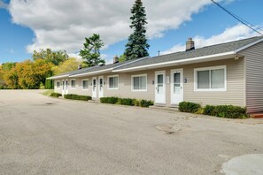 A row of single-story motel buildings with numbered doors, a paved driveway, and a backdrop of trees and a clear sky. - Waterfront Lake Huron Condo at Sunrise Side Resort (Greenbush)
