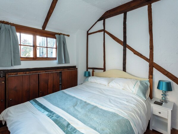 A bedroom with a wooden headboard, a bed with a striped bedspread, a nightstand with a lamp, and a window with curtains. - Barnaby's Lodge - UK51951 (Broadstairs)