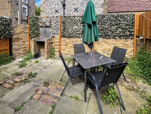 A patio with a table and chairs, a green umbrella, and a brick wall with climbing plants. - Barnaby's Lodge - UK51951 (Broadstairs)
