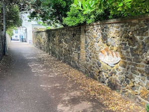 A stone wall with a carved stone piece, a paved path, and trees. - Barnaby's Lodge - UK51951 (Broadstairs)