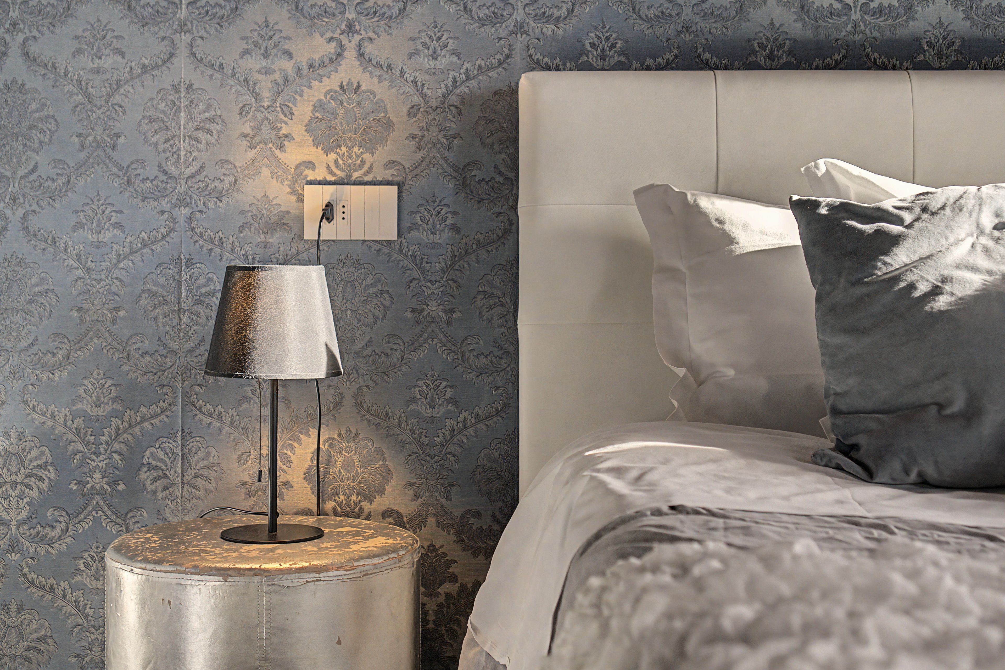 Une chambre à coucher avec un lit, une table de chevet avec une lampe et un mur recouvert d’un papier peint à motifs.