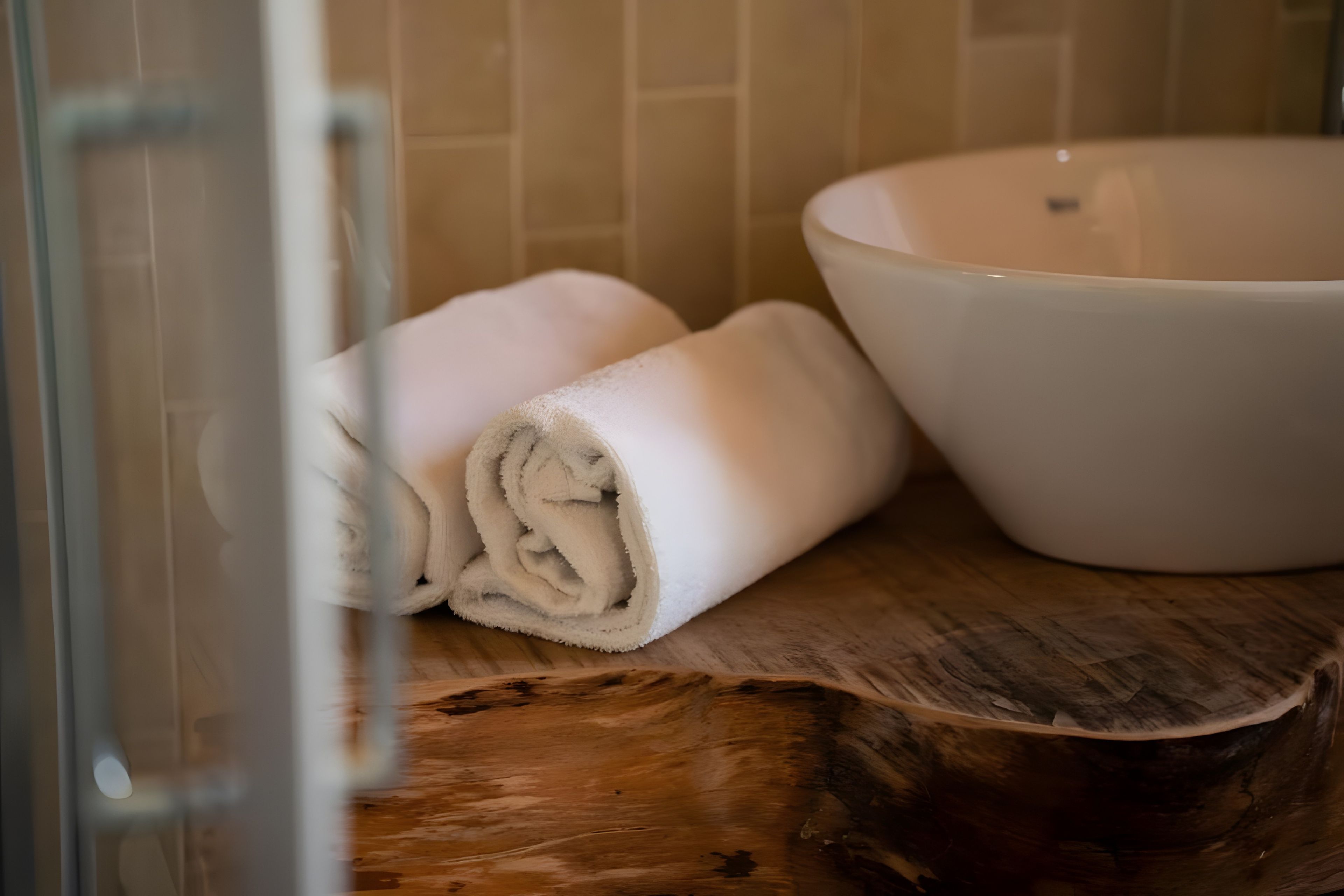 Ein Badezimmer mit einem Holzwaschtisch, einer weißen Keramikschale und aufgerollten Handtüchern.