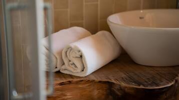 Ein Badezimmer mit einem Holzwaschtisch, einer weißen Keramikschale und aufgerollten Handtüchern.