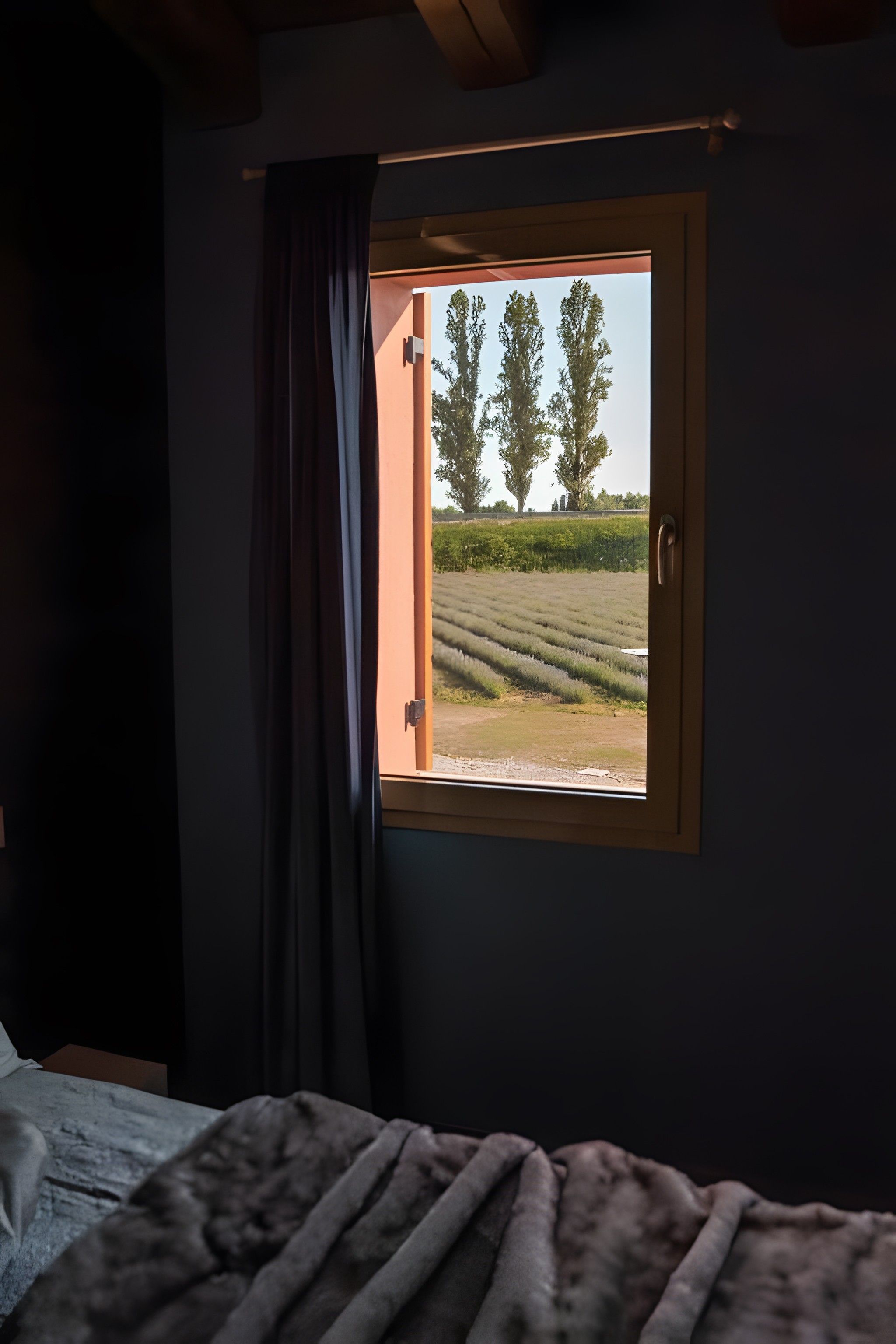Ein Schlafzimmer mit einem Fenster, das auf ein Feld und Bäume blickt.