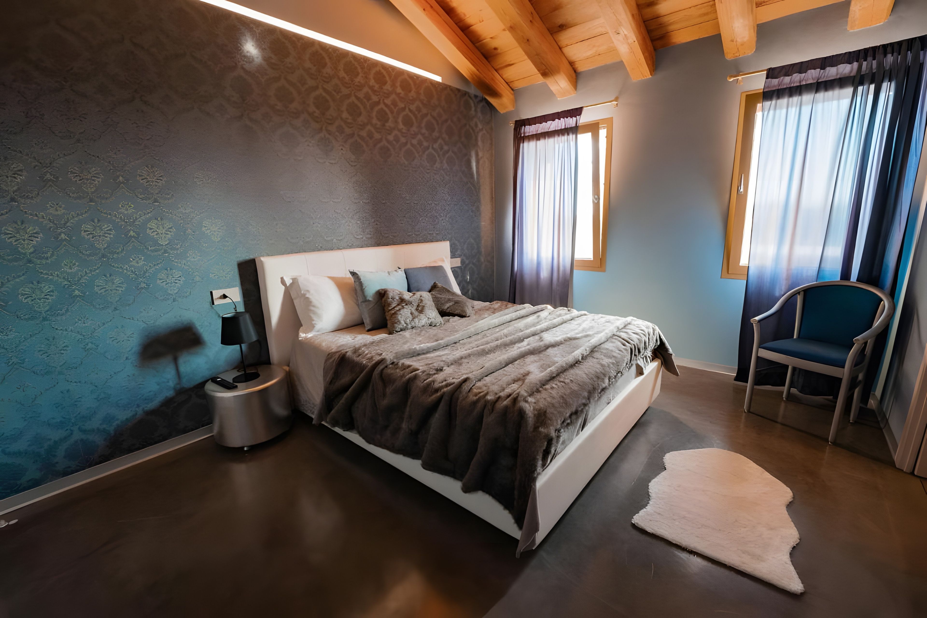 Ein Schlafzimmer mit Bett, Nachttisch, Lampe, Stuhl und Teppich.