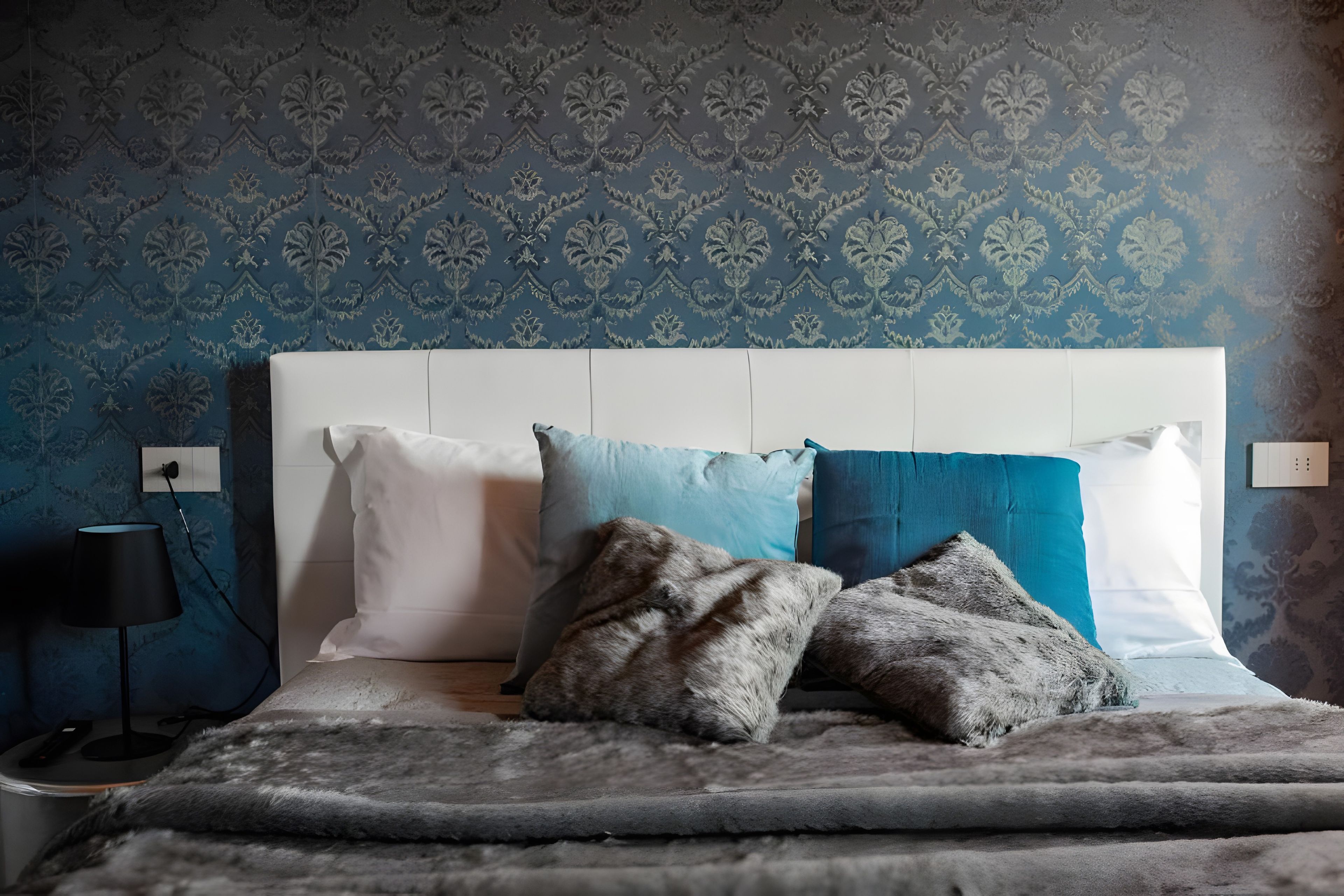 Ein Schlafzimmer mit strukturierter Tapete, einem weißen Kopfteil und einem Bett mit vielen Kissen.