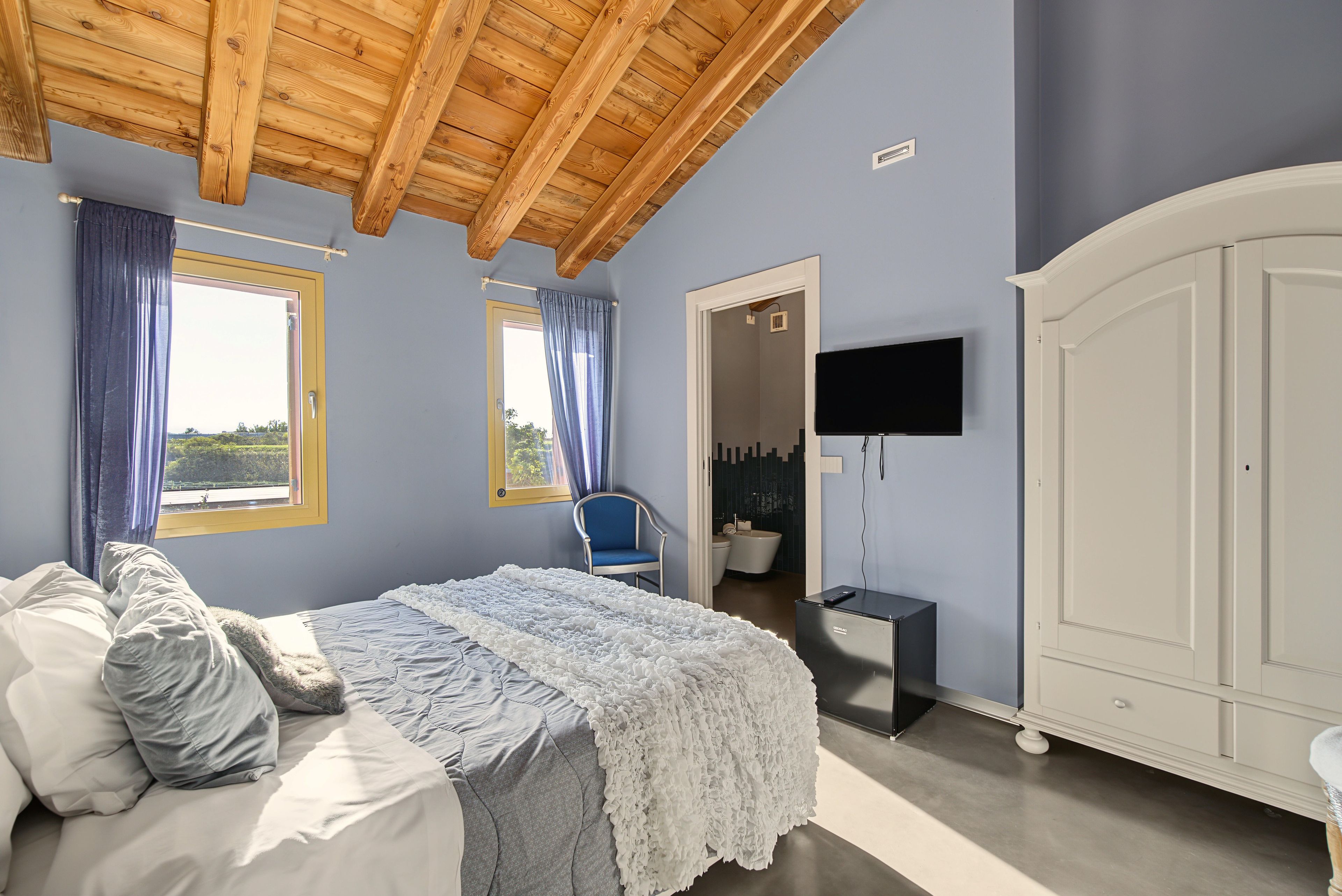 A bedroom with a bed, a wardrobe, a television, and a bathroom visible through an open door.