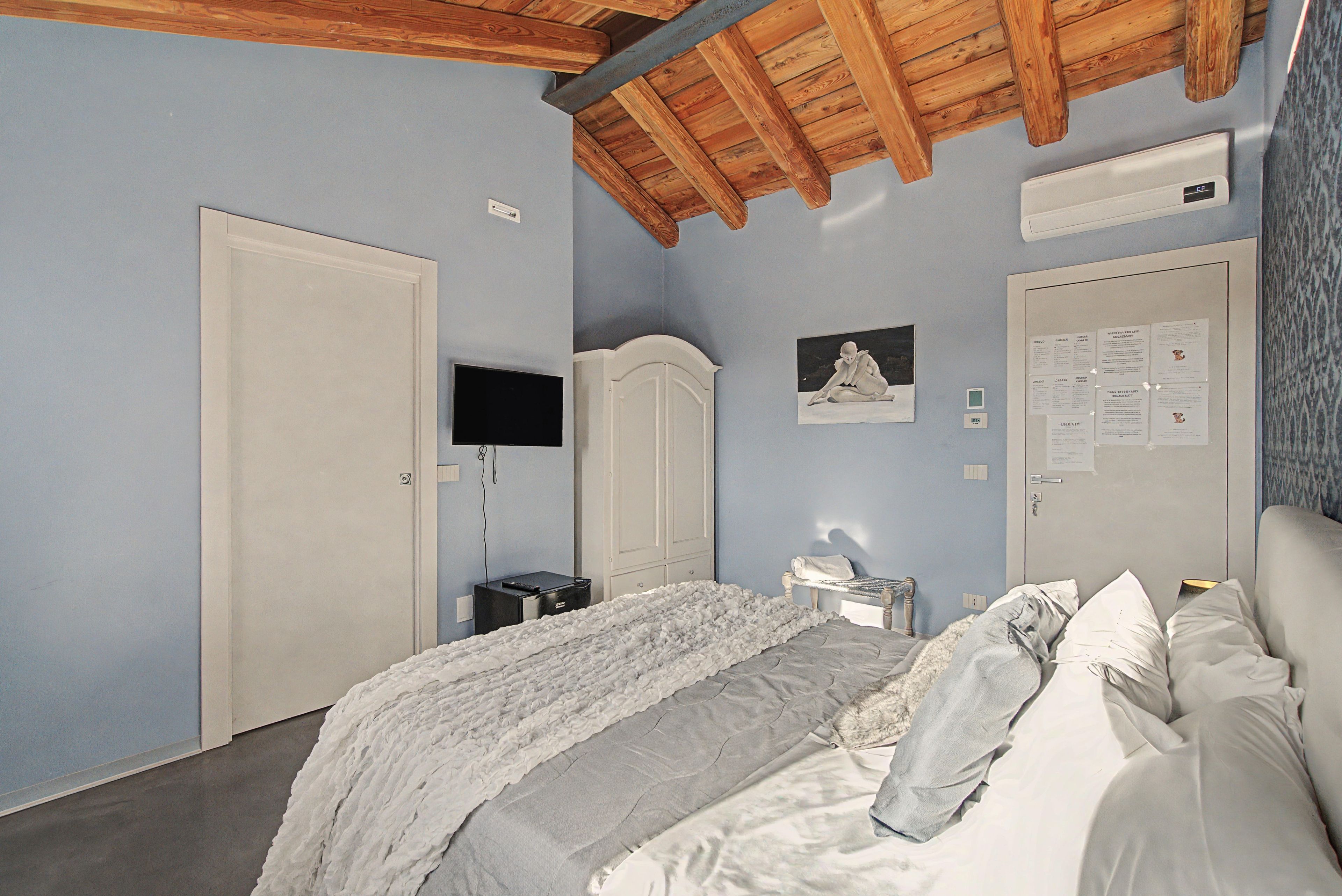 A bedroom with a bed, a wardrobe, a television, and a wall-mounted air conditioner.