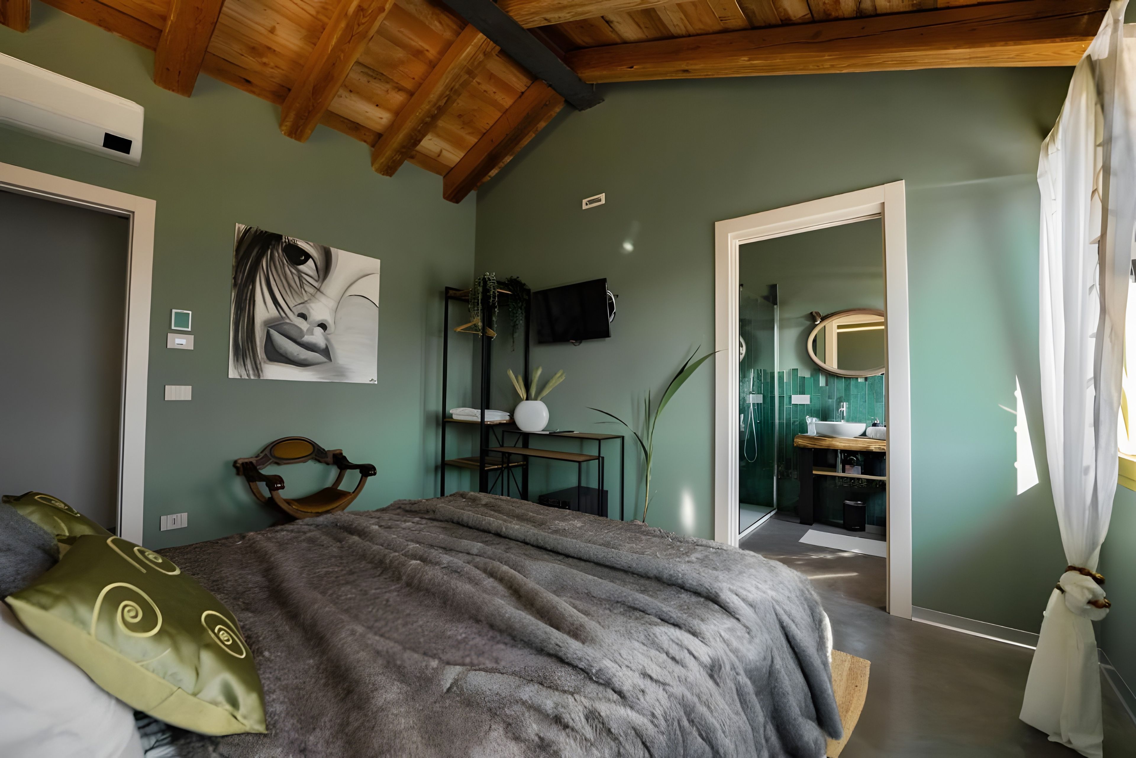 Een slaapkamer met een bed, een schilderij, een bureau en een badkamer zichtbaar door een geopende deur.