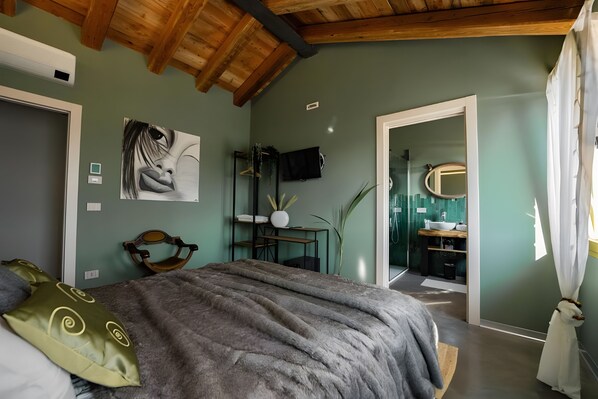 Een slaapkamer met een bed, een schilderij, een bureau en een badkamer zichtbaar door een geopende deur.
