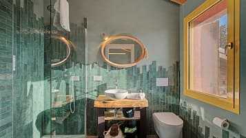 Ein Badezimmer mit Duschkabine aus Glas, einem Holzkosmetikschrank mit Waschbecken und einer Toilette, sowie einem Fenster mit Blick.