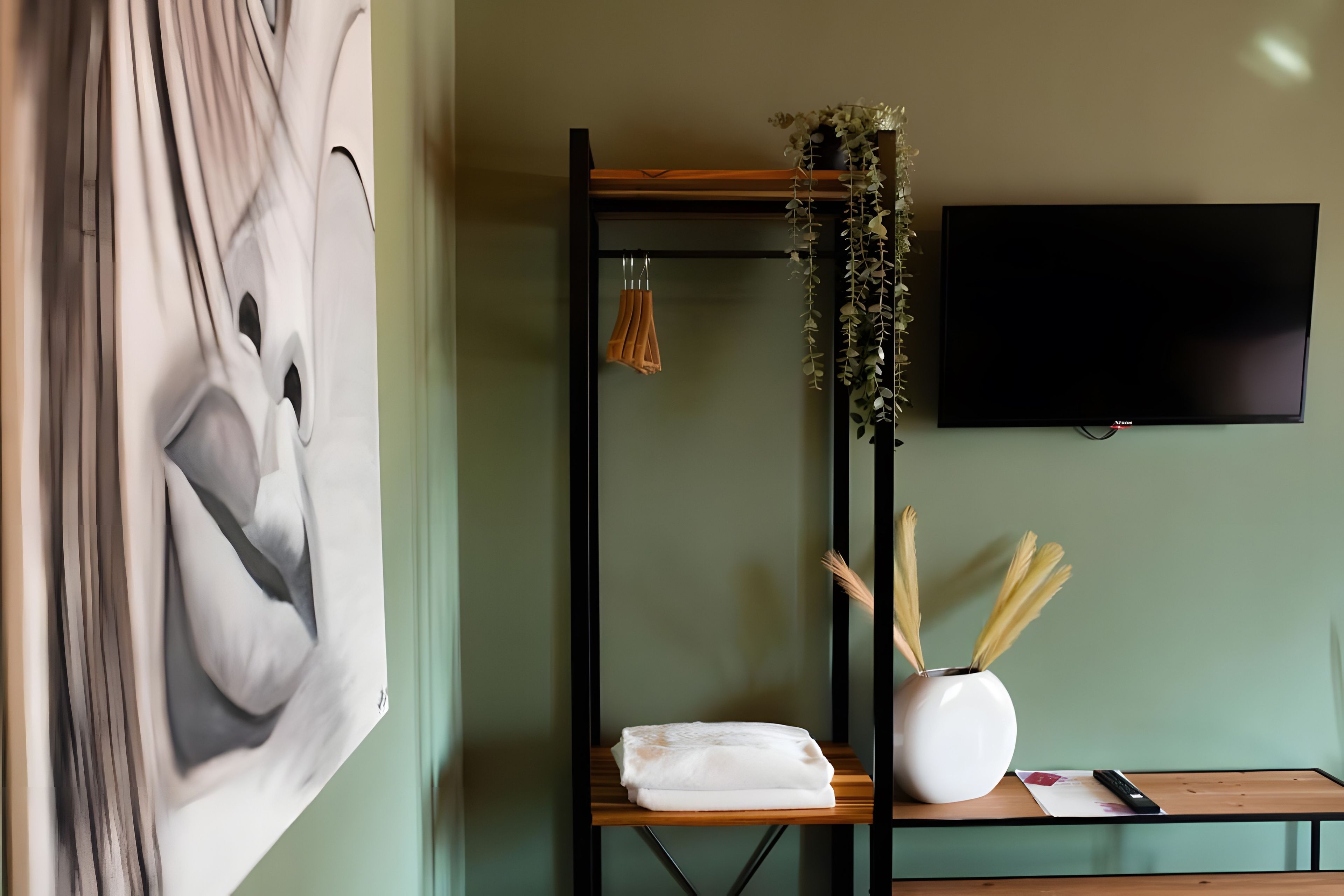 Ein Zimmer mit einem großen abstrakten Gemälde, einem an der Wand montierten Fernseher, einem Holzregal mit einer Vase und Dekoration sowie einem Bett mit weißer Decke.