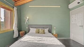Une chambre à coucher avec un lit, une table de chevet, une lampe fixée au mur et une fenêtre avec des rideaux.