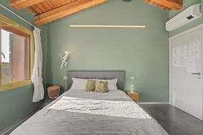 A bedroom with a bed, a nightstand, a wall-mounted lamp, and a window with curtains.