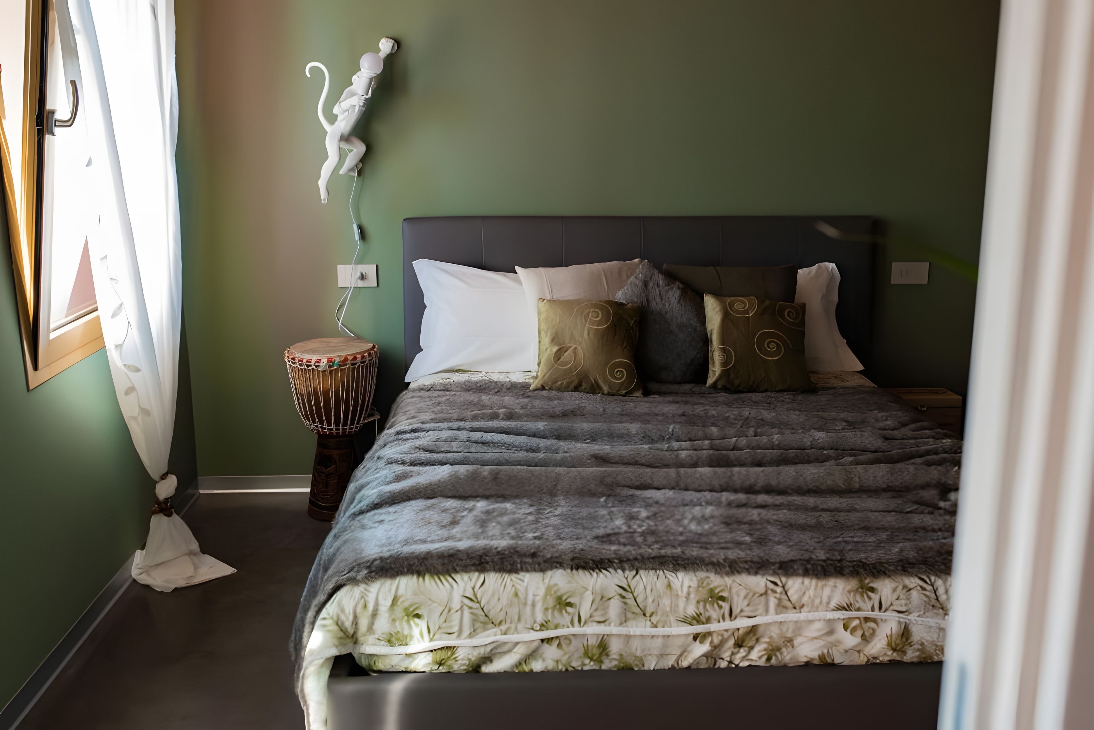 Een slaapkamer met een bed, een trommelstoel en een sculptuur aan de muur.