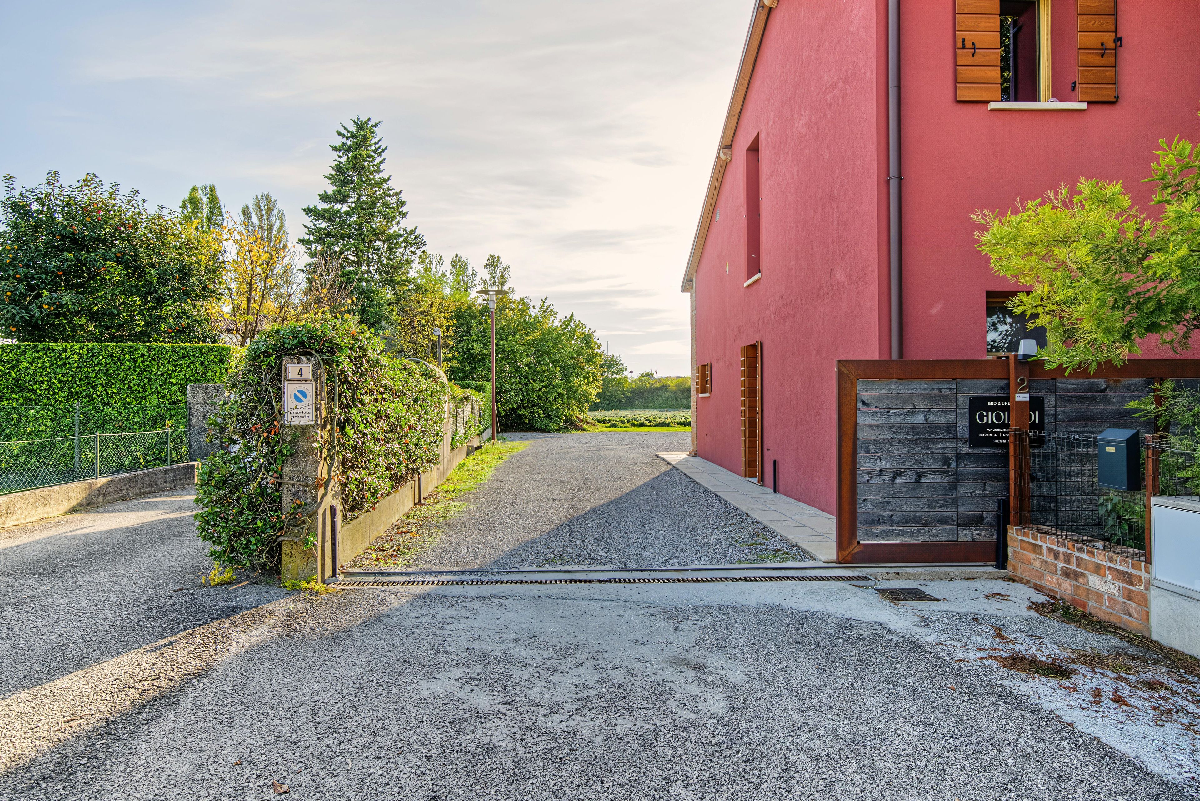 A gravel driveway leading to a red building with a wooden door and a window with shutters.