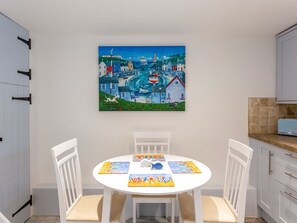 Ein Essbereich mit einem runden Tisch, weißen Stühlen und einem farbenfrohen Gemälde einer Küstenstadt an der Wand.