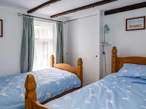 Ein Schlafzimmer mit zwei Holzbetten, einem Fenster mit Vorhängen, einer Wandlampe und einem gerahmten Bild.