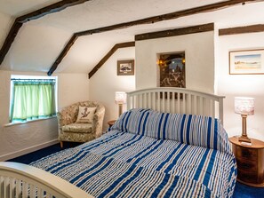 A bedroom with a sloped ceiling, a bed with a striped bedspread, a chair with a floral cushion, and two wall-mounted lamps. - Smuggler's Cottage - UK51952 (Broadstairs)
