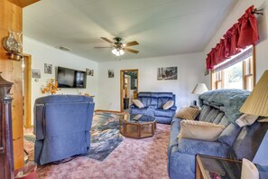 A living room with a ceiling fan, a television, a blue sofa, a coffee table, and a fireplace. - Streamside Tallmansville Retreat: Fish & Unwind (Tallmansville)