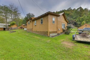 A wooden cabin with a fenced yard, a truck, and a mailbox. - Streamside Tallmansville Retreat: Fish & Unwind (Tallmansville)