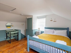 Quarto com cama, escrivaninha, espelho e janela.