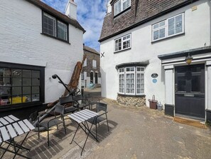 A courtyard with outdoor seating, a stone wall, and a building with a black door and a sign indicating a cottage. - Old Anchor Cottage - UK51953 (Broadstairs)