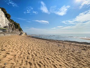 Une plage avec une falaise rocheuse, un rivage sablonneux et un ciel dégagé.