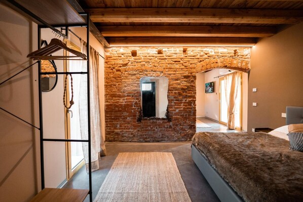 Een slaapkamer met een stenen muur, een bed, een houten plafond en een raam.