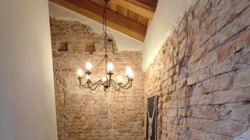 Una stretta scala con pareti in mattoni a vista, soffitto in legno e lampadario pendente.