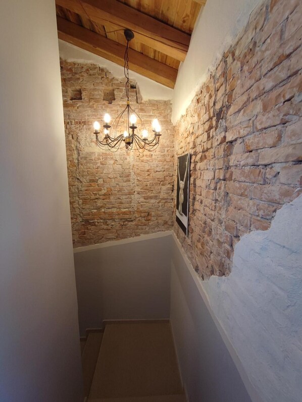 A narrow staircase with exposed brick walls, a wooden ceiling, and a hanging chandelier. - Room 'Gioia Di - King Superior' with shared garden, Wi-Fi and air conditioning (Biverone)