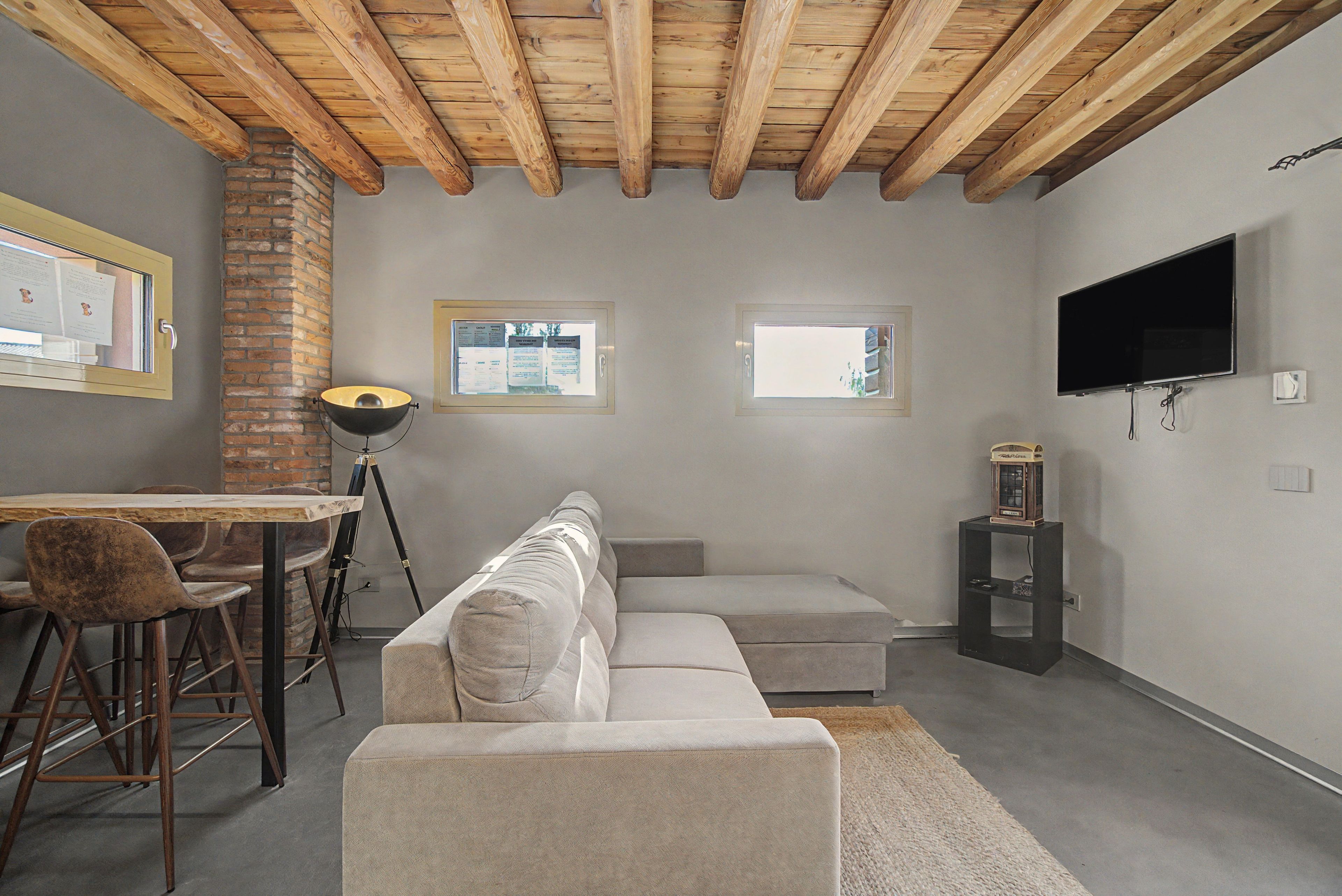 Un salon moderne avec un plafond en bois, un canapé, un téléviseur et un bureau avec une lampe.