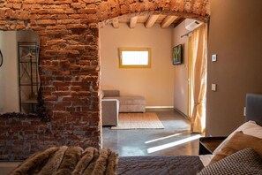 Een kamer met openliggende bakstenen muren, een raam met een gele omlijsting, een bank en een bed met een bedspread met een patroon.