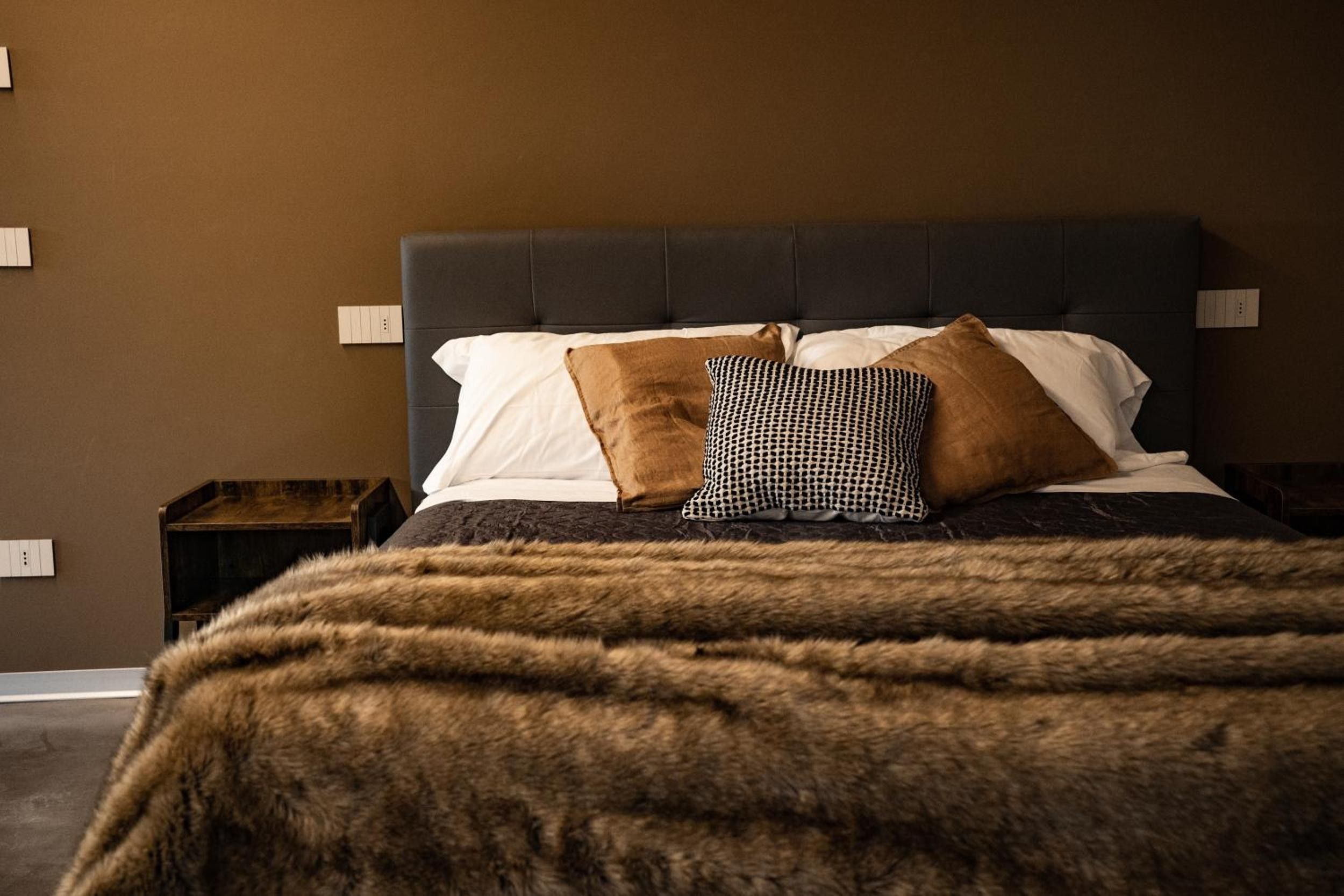 Ein Bett mit dunklem Kopfteil, weißen, gemusterten Kissen und einem Fellüberwurf.