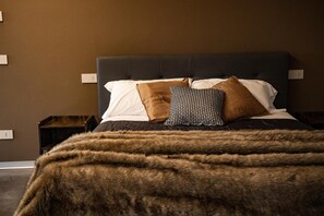 Een bed met een donker hoofdbord, witte en gestreepte kussens, en een bont plaid.