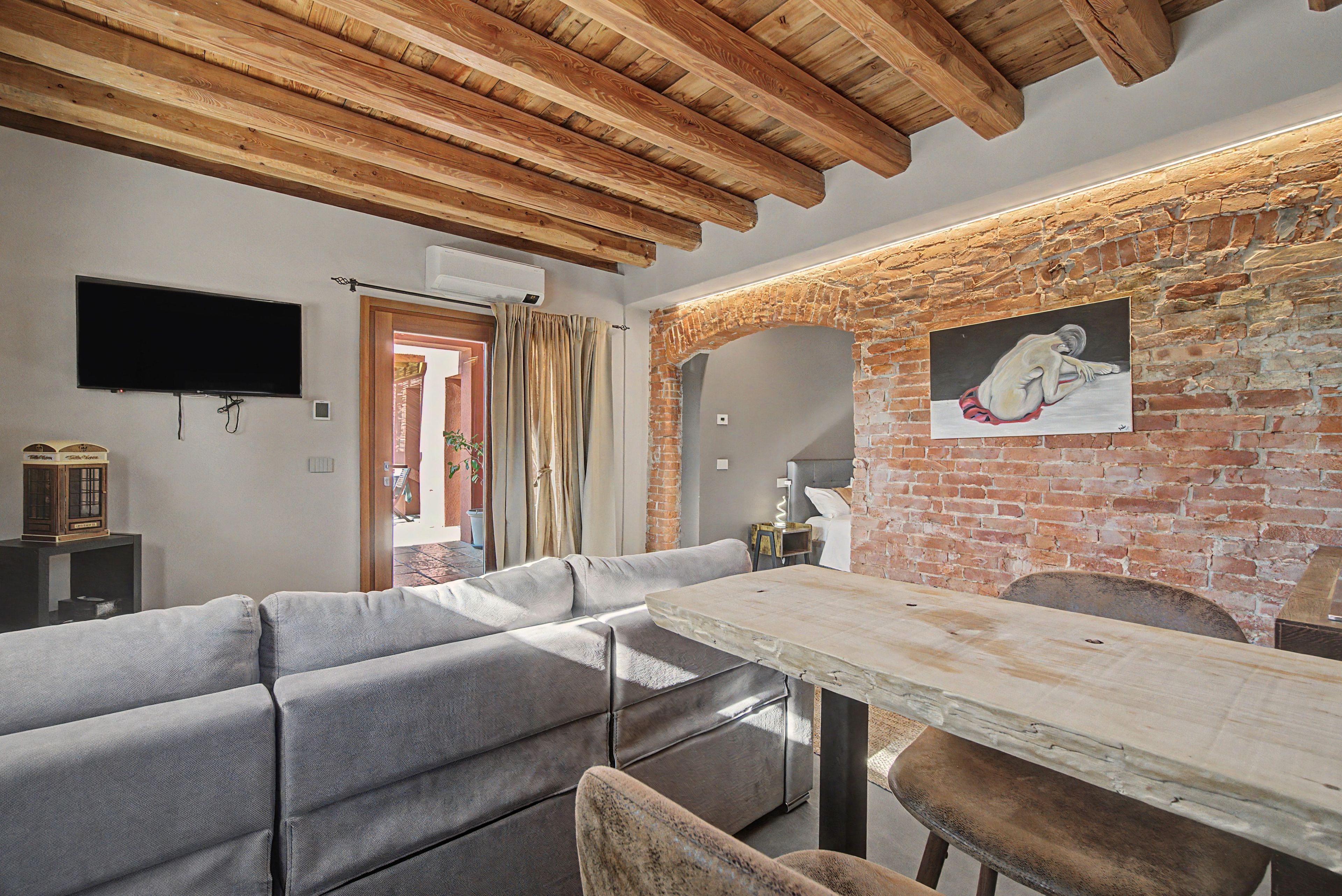 Un salon moderne avec un plafond en bois, un mur en briques, un téléviseur à écran plat, un canapé et une table à manger.