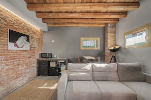 A cozy living area with a sofa, a small kitchenette, and a brick wall.