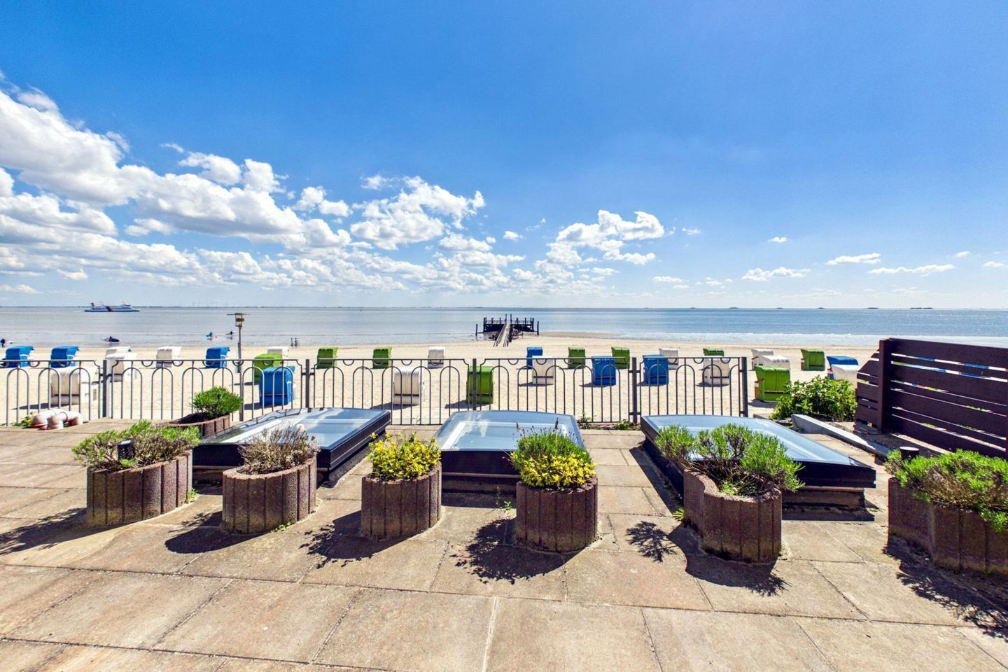 Une propriété située en bord de mer, avec une rangée de chaises longues et des jardinières, une vue dégagée sur la mer et un navire visible au loin.