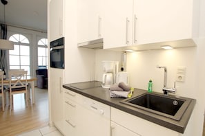 A modern kitchen with white cabinets, a black countertop, a sink, a coffee maker, and a kettle. - Sandwall 19, Apt. No. 22, Nordstrand Nordland Apartments - Vacation Rental with 2- (Wyk auf Föhr)