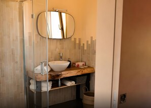 Een badkamer met een glazen douchecabine, een ronde spiegel, een wit wastafelmeubel en een houten kast.