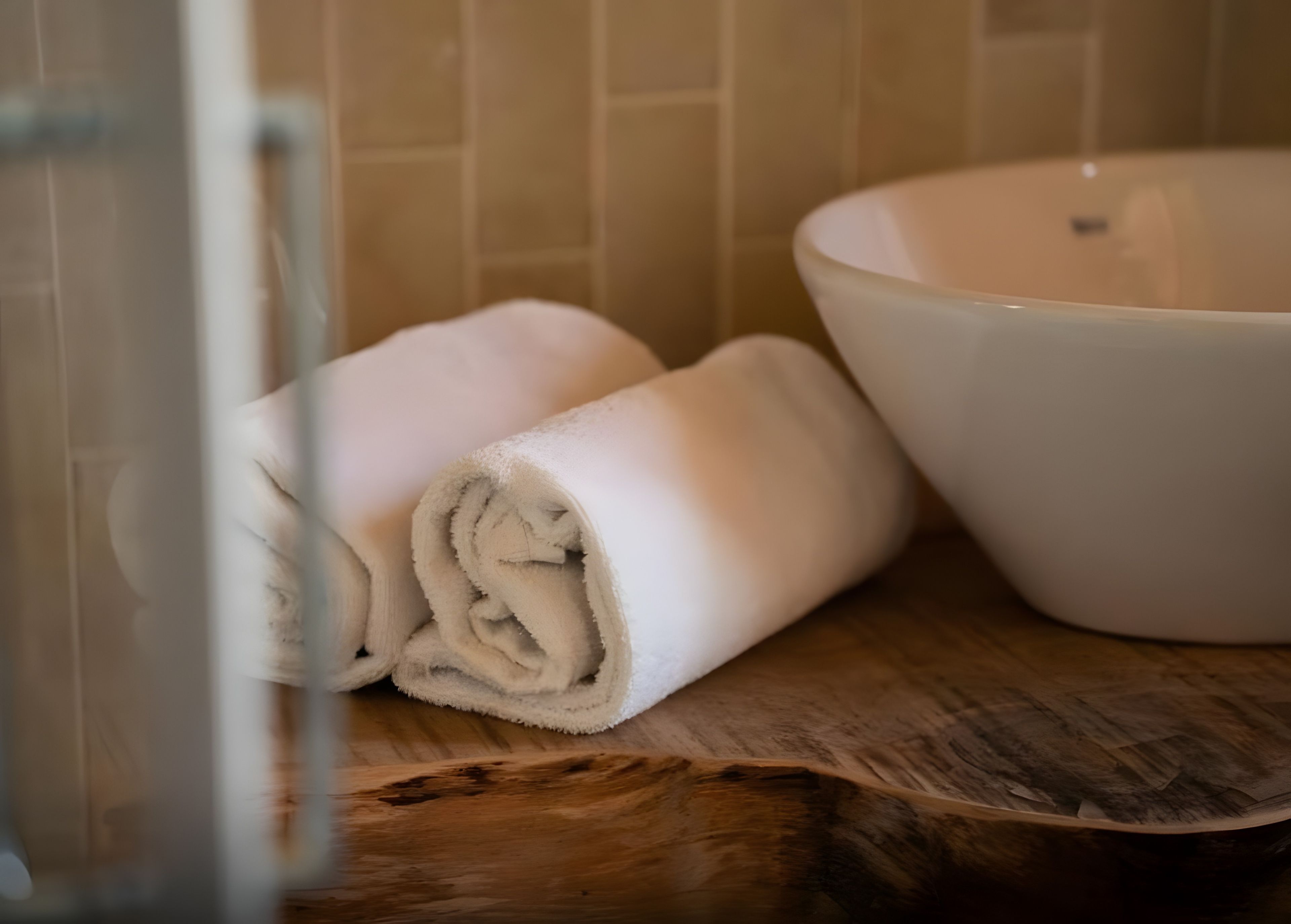 Ein Badezimmer mit Waschtisch aus Holz, einer weißen Schüssel und gerollten Handtüchern.